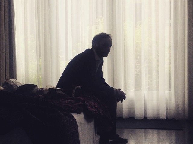 Hombre sentado en el borde de la cama en una habitación en penumbra, reflejando el estado de hipervigilancia o rumiación por ansiedad.