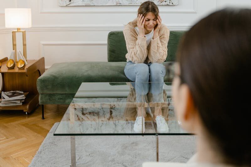 A distressed woman sitting on a green sofa during a therapy session indoors.