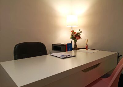 Escritorio de psicólogo iluminado por una lámpara de mesa cálida, con un jarrón de flores, un bolígrafo sobre documentos y sillas de consulta.