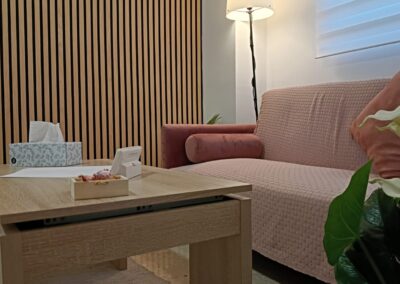 Primer plano de una planta de interior junto a una mesa auxiliar de madera y un cómodo sofá en una consulta de psicología iluminada.